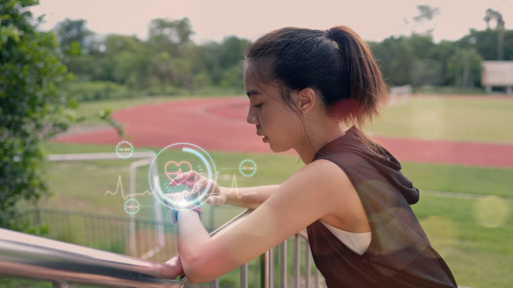 A woman wearing a smart watch is standing on a grassy field